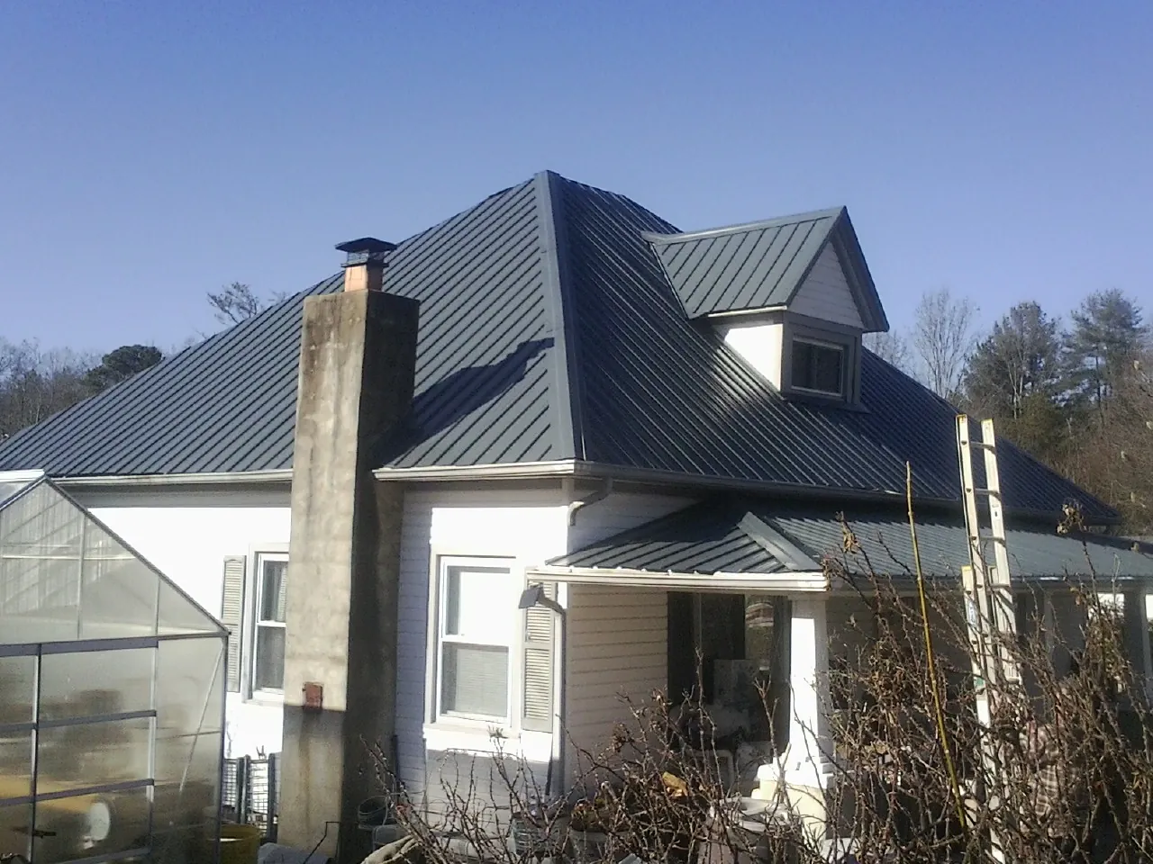 Dark blue standing seam metal roof on a white farmhouse with dormer — Slate & Tile Roof Repair by Roofing Brothers in Peterborough