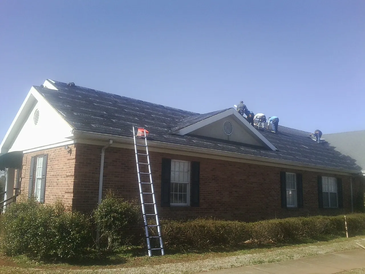 Crew tearing shingles off a brick ranch roof with a ladder set — Emergency Roof Repair work by our crew in Peterborough