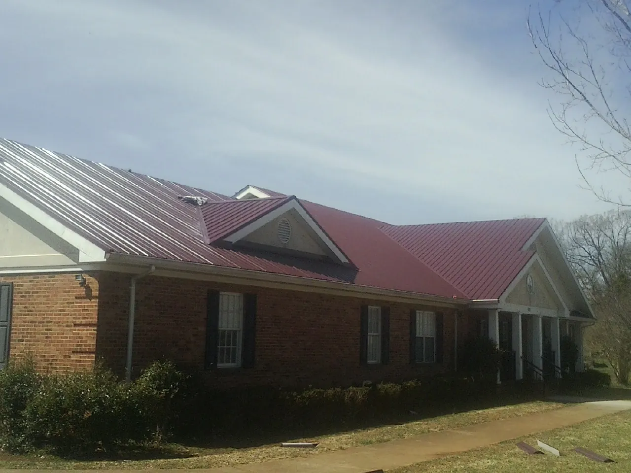 Red metal roof with gabled entries on a long brick building, from a Hail Damage Roof Repair job in Peterborough