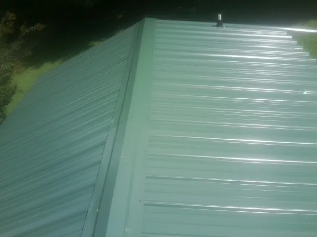 New green metal panels meeting at the ridge of a roof — Flat Roof Repair work by our crew in Peterborough