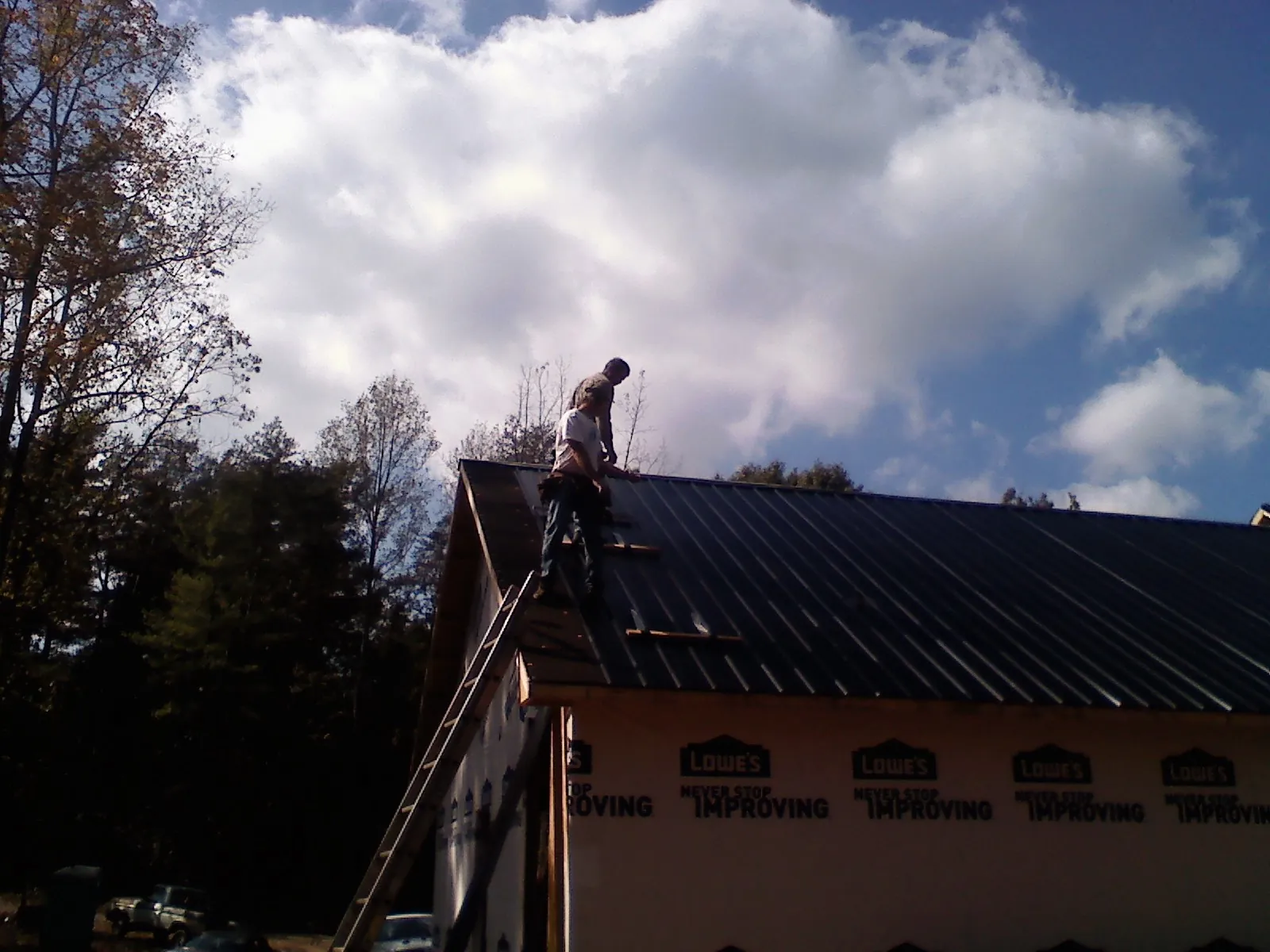 Roofer fastening dark metal panels high against a cloudy sky, from a Roof Inspection job in Peterborough