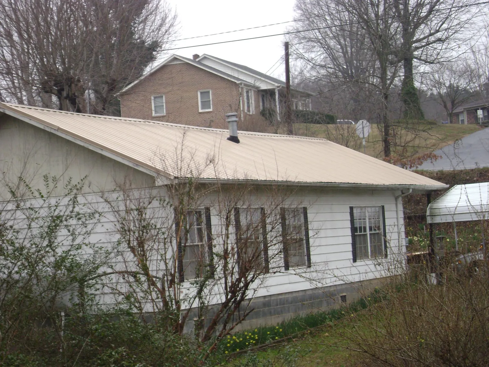 Tan metal roof on a white sided house set into a hillside — Commercial Roofing by Roofing Brothers in Peterborough