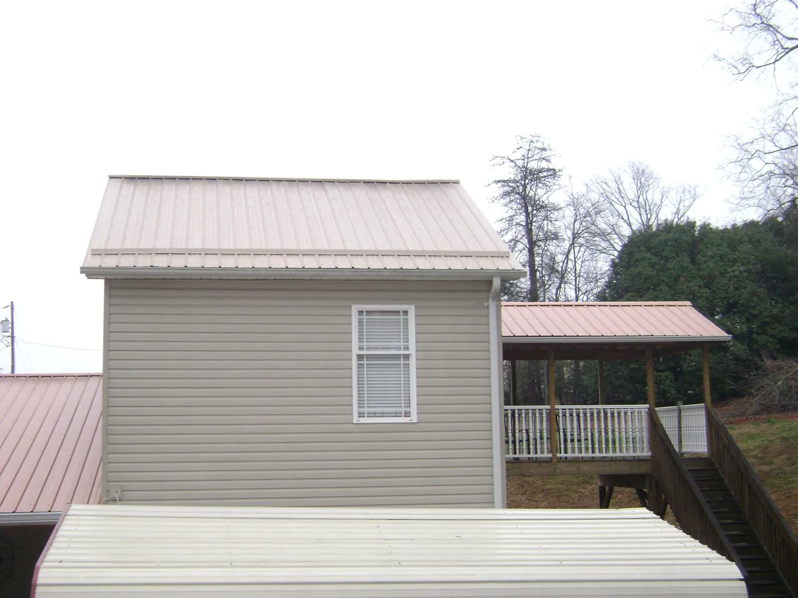 Tan metal roofs on a two story addition and attached porch, from a Roof Replacement job in Peterborough